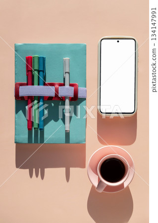 Notebook with colorful markers, coffee cup and smartphone with blank screen, top view. Notebook with colorful markers, coffee cup and smartphone with blank screen, top view. 134147991
