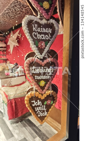 This festive photo captures a set of traditional German gingerbread hearts (Lebkuchenherzen) hanging in a Christmas market stall. Decorated with colorful icing and loving messages in German This festive photo captures a set of traditional German gingerbread hearts (Lebkuchenherzen) hanging in a Christmas market stall. Decorated with colorful icing and loving messages in German 134148545