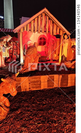 A beautifully illuminated nativity scene displayed outdoors at night, depicting the birth of Jesus Christ. The wooden stable is surrounded by detailed statues of Mary, Joseph, the Three Wise Men A beautifully illuminated nativity scene displayed outdoors at night, depicting the birth of Jesus Christ. The wooden stable is surrounded by detailed statues of Mary, Joseph, the Three Wise Men 134148546