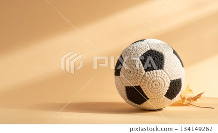 A hand-knitted wool soccer ball with its finely woven yarn is placed against a warm caramel matte background. 134149262