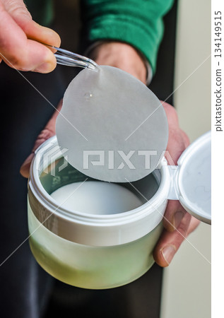 Cosmetic Toner Pad Held Above Open Skincare Jar 134149515