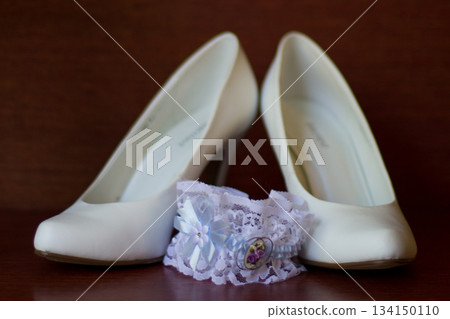 Elegant white wedding shoes and garter on wooden table Elegant white wedding shoes and garter on wooden table 134150110