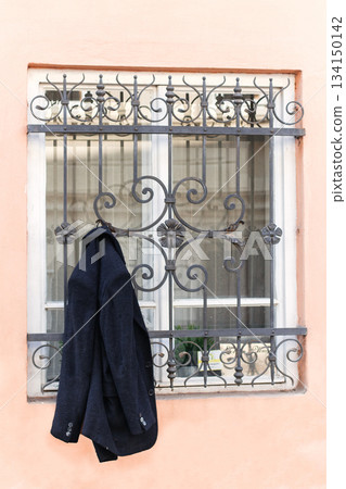 Groom's jacket hanging from a window with decorative metal bars during wedding preparations Groom's jacket hanging from a window with decorative metal bars during wedding preparations 134150142