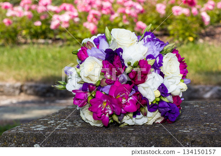 Colorful wedding bouquet resting on stone with roses in background Colorful wedding bouquet resting on stone with roses in background 134150157