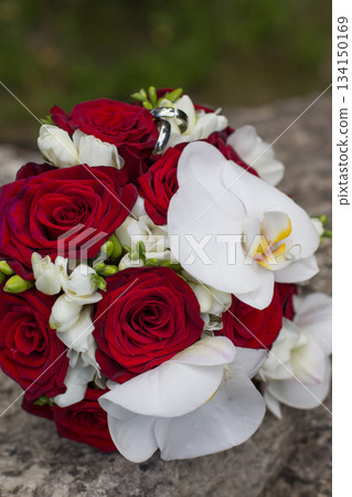 Wedding rings resting on a bridal bouquet of red roses and white orchids 134150169