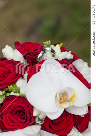 Wedding rings resting on a bouquet of red roses and white orchids Wedding rings resting on a bouquet of red roses and white orchids 134150173