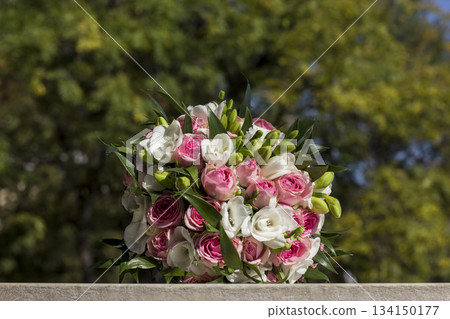 Wedding bouquet resting on stone surface with blurred foliage background Wedding bouquet resting on stone surface with blurred foliage background 134150177