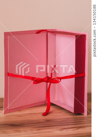 Pink wedding gift box tied with red ribbon bow on wooden table Pink wedding gift box tied with red ribbon bow on wooden table 134150186