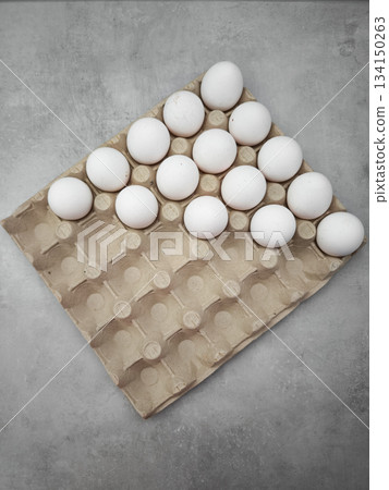 White eggs filling half of cardboard egg carton on gray table easter 134150263