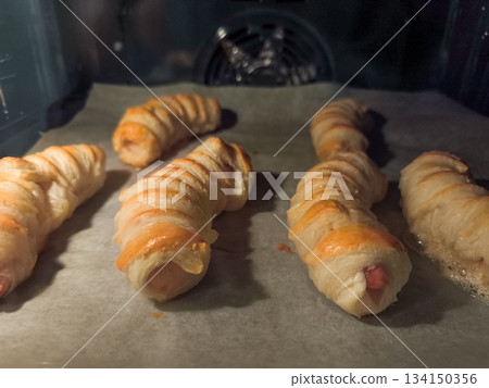 Veal sausage rolls in puff pastry baking in oven on parchment paper 134150356