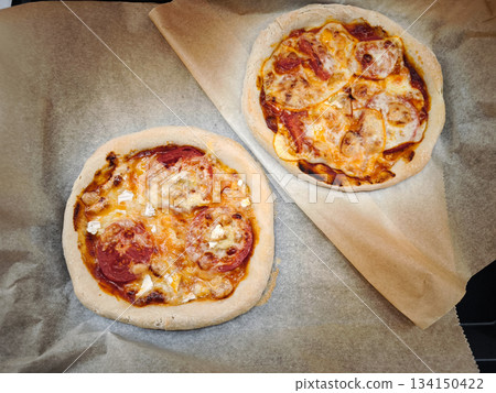 Two mini pizzas baking on parchment paper with tomato and cheese Two mini pizzas baking on parchment paper with tomato and cheese 134150422