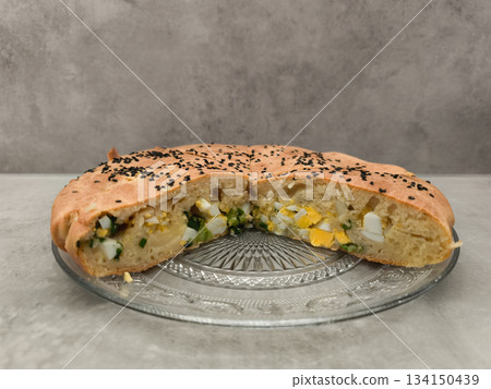 Savory easter pie with eggs and spring onions, sprinkled with black sesame seeds copy space gray background Savory easter pie with eggs and spring onions, sprinkled with black sesame seeds copy space gray background 134150439