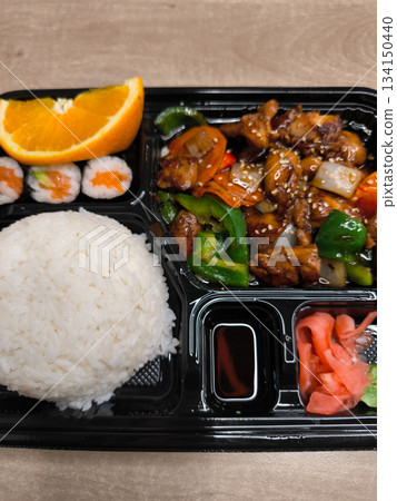Bento box filled with rice, teriyaki chicken, sushi, orange slice, and pickled ginger lunch fast food Bento box filled with rice, teriyaki chicken, sushi, orange slice, and pickled ginger lunch fast food 134150440