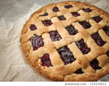 Homemade cherry pie cooling on rustic parchment, golden crust showcasing sweet seasonal filling Homemade cherry pie cooling on rustic parchment, golden crust showcasing sweet seasonal filling 134150612