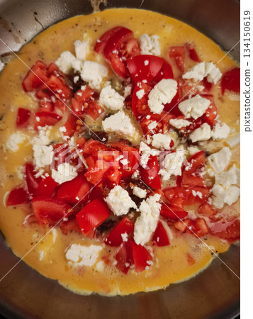 Valentine's day morning, cooking fluffy omelette with ripe tomatoes, melting goat cheese in sizzling skillet 134150619