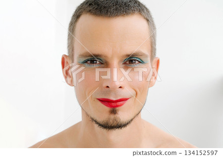 portrait of a happy feminine gay man with makeup and cosmetics on face. A handsome young transgender male with red lipstick and eye shadow sparkle on his eyes on a white background portrait of a happy feminine gay man with makeup and cosmetics on face. A handsome young transgender male with red lipstick and eye shadow sparkle on his eyes on a white background 134152597