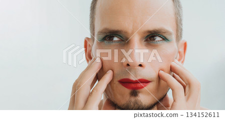 portrait of a feminine gay man with makeup and cosmetics on his face. Handsome adult transgender male with red lipstick on lips and mascara on eyes on white background portrait of a feminine gay man with makeup and cosmetics on his face. Handsome adult transgender male with red lipstick on lips and mascara on eyes on white background 134152611
