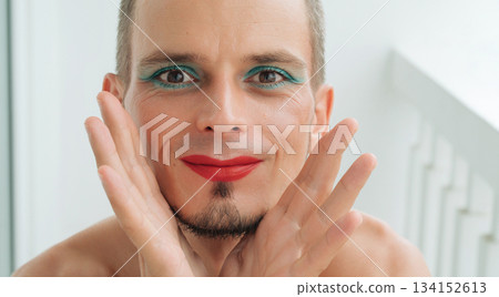 portrait of happy gay man with makeup and cosmetics on face. A white man with red lipstick on lips and mascara on eyes portrait of happy gay man with makeup and cosmetics on face. A white man with red lipstick on lips and mascara on eyes 134152613