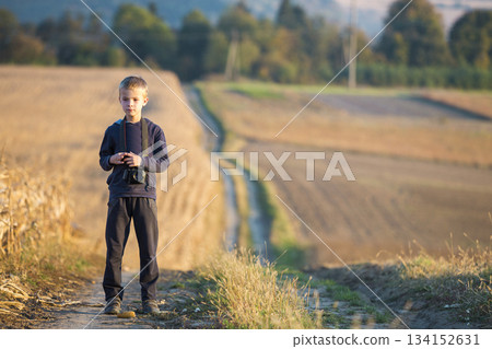 Young child boy with photo camera at wheat field on blurred rural background. 134152631
