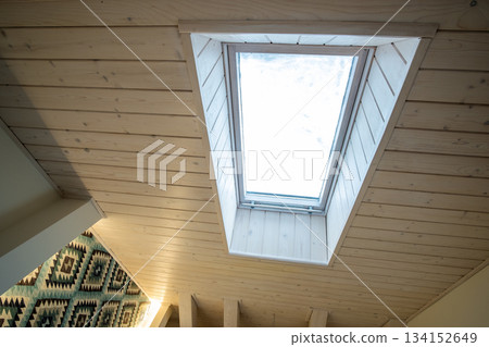 Wooden ceiling in a contemporary mansard room with attic window ob decorative planks surface. 134152649