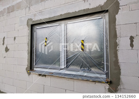 Window of a house under construction covered with protective plastic film. 134152660