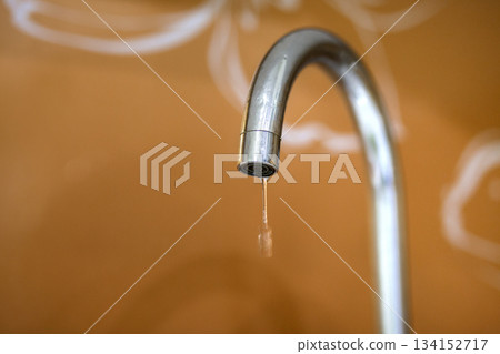 Water tap, chrome stainless metal faucet with running stream of water in bathroom or kitchen, mixer cold hot water isolated on bright yellow copy space background. Modern kitchen interior. Water tap, chrome stainless metal faucet with running stream of water in bathroom or kitchen, mixer cold hot water isolated on bright yellow copy space background. Modern kitchen interior. 134152717