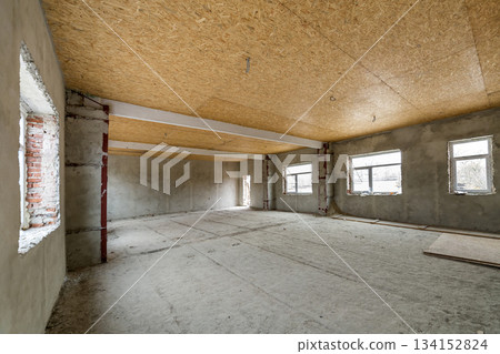 Unfinished apartment or house big loft room under reconstruction. Plywood ceiling, plastered walls, window openings, cement floor. Construction and renovation concept. Unfinished apartment or house big loft room under reconstruction. Plywood ceiling, plastered walls, window openings, cement floor. Construction and renovation concept. 134152824
