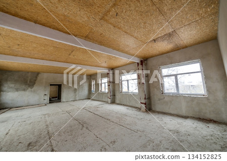 Unfinished apartment or house big loft room under reconstruction. Plywood ceiling, plastered walls, window openings, cement floor. Construction and renovation concept. 134152825