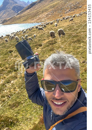 A man with a camera is posing with a herd of sheep in the background A man with a camera is posing with a herd of sheep in the background 134153435