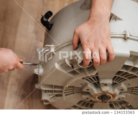 Mechanic repairing a washing machine drum, showing hands-on appliance maintenance at work. Mechanic repairing a washing machine drum, showing hands-on appliance maintenance at work. 134153563