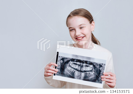 Smiling little girl holding a dental x-ray on a white background, representing child dental care and oral health 134153571