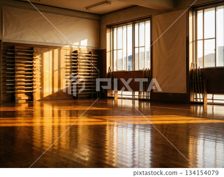 Sunlight streams through large windows into a dojo with a polished wooden floor. The walls feature shelves and reflections create a warm atmosphere for training. 134154079