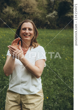 Happy middle-aged woman enjoying nature and embracing herself in spring field. Concept of self-love, female health, emotional balance, mindfulness, and positive aging Happy middle-aged woman enjoying nature and embracing herself in spring field. Concept of self-love, female health, emotional balance, mindfulness, and positive aging 134154471