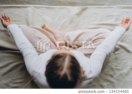 Smiling woman practicing yoga at home, doing seated forward bend on a mat. Healthy lifestyle, flexibility, self care, and balance in a peaceful home environment 134154485