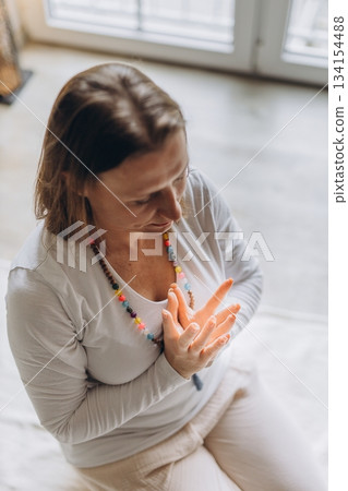 Calm woman practicing kundalini yoga at home in prayer pose. Mindfulness, inner peace, and healthy lifestyle in serene morning light 134154488