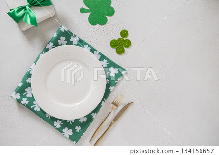 St Patricks day empty table setting with white plate, green shamrock napkin and gold cutlery on light background. Flat lay with copy space. 134156657