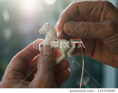 Hands are shown attaching a small white porcelain horse to a thin string. This scene captures a moment of preparation for New Year's celebrations with a festive spirit. Hands are shown attaching a small white porcelain horse to a thin string. This scene captures a moment of preparation for New Year's celebrations with a festive spirit. 134156989