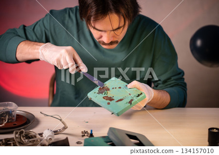 Craftsman using putty knife tool and scraping off old paint from base part of electric lamp. 134157010