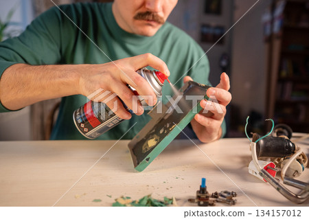 Crafter spraying paint stripper from spray can on metallic surface of lamp base to remove old paint. Crafter spraying paint stripper from spray can on metallic surface of lamp base to remove old paint. 134157012