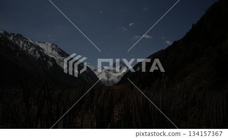 Majestic mountain landscape with snow-capped peaks and dark valley Majestic mountain landscape with snow-capped peaks and dark valley 134157367
