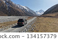 SUV driving on gravel road through mountainous landscape with clear sky 134157379