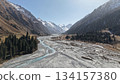 Scenic mountain river flowing through valley with majestic peaks in background 134157380