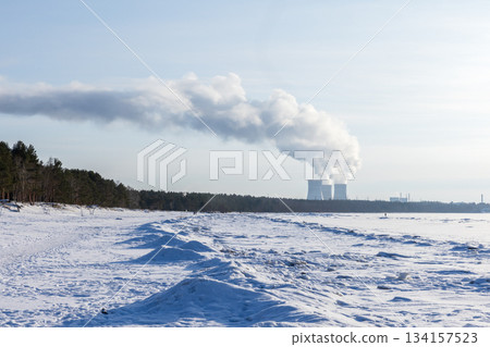 A tranquil, snowy beach sits beside a forest edge while a distant power plant A tranquil, snowy beach sits beside a forest edge while a distant power plant 134157523