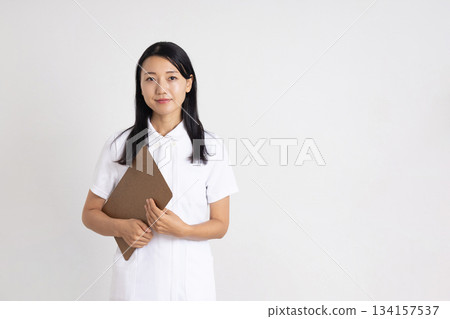 A woman in a white coat smiling while holding a binder in front of a white background A woman in a white coat smiling while holding a binder in front of a white background 134157537