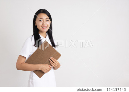 A woman in a white coat smiling while holding a binder in front of a white background 134157543