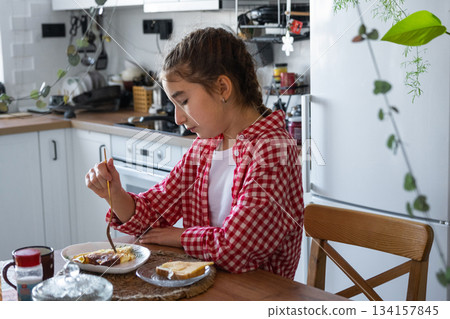 The girl has breakfast in the kitchen with scrambled eggs and a sandwich at the table in the morning 134157845