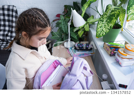 The girl packs her backpack for school in the morning, puts down her textbooks The girl packs her backpack for school in the morning, puts down her textbooks 134157852