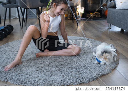 A girl plays with a domestic cat on a carpet with a fishing rod with a worm 134157874