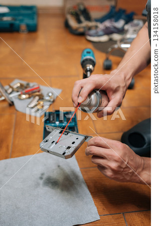 Vertical shot of carpenter male lubricating door lock mechanism with spray oil, performing home maintenance or diy repair work to prevent sticking and extend hardware lifespan in domestic setting. 134158018