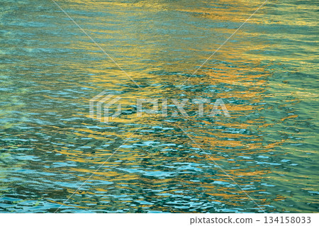 Reflection of city light on water at night. Night sea view with street light. Light hitting on the ocean.Sea background. Background of the calm water, water waves. Sea water surface. Reflection of city light on water at night. Night sea view with street light. Light hitting on the ocean.Sea background. Background of the calm water, water waves. Sea water surface. 134158033